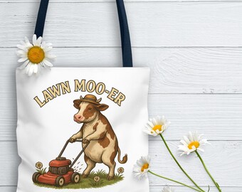 May include: White tote bag with a navy blue handle featuring a cartoon cow mowing the lawn. The cow wears a hat and the text "LAWN MOO-ER" is arched above the cow. Daisies are placed around the bag.