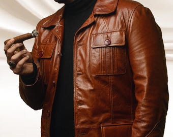 May include: A brown leather jacket with a collared neckline, buttoned front, and multiple pockets. The jacket has a vintage style and a worn appearance. The person is wearing a black turtleneck. The jacket has a classic, timeless design.