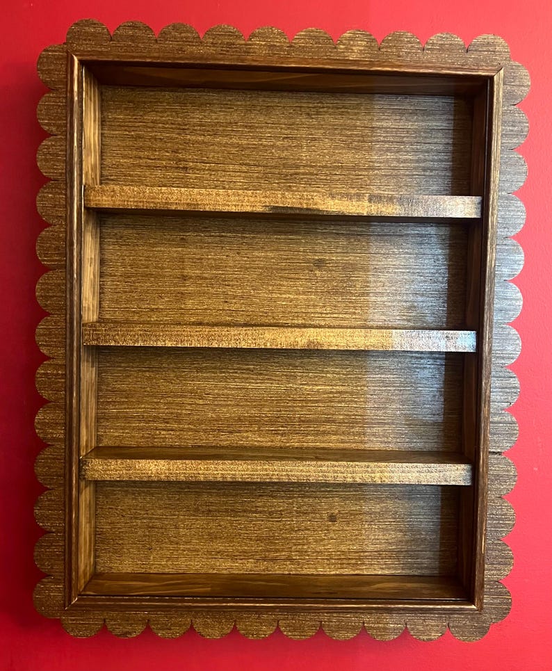 May include: A wooden wall shelf with four horizontal shelves. The frame has a scalloped edge. The wood has a warm brown stain, and the shelves are evenly spaced within the rectangular frame. The shelf is designed for displaying small items.
