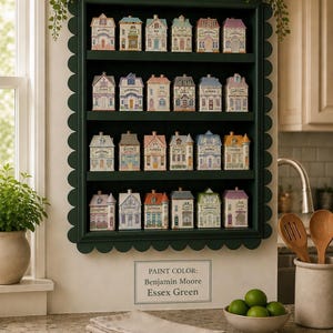 May include: A dark green scalloped shelf displays a collection of miniature, colorful ceramic houses. Each house is uniquely designed and labeled with a spice name. The shelf is adorned with floral accents, creating a charming kitchen display.