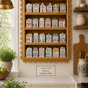 May include: A wooden shelf with a scalloped edge displays miniature ceramic houses, each painted with unique colors and architectural details. The shelf is stained with Minwax Golden Oak. The houses are arranged in rows, creating a charming decorative display.