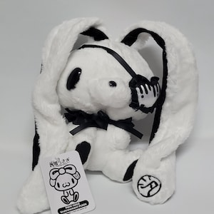 May include: A white plush rabbit with long ears, black accents, and a black eye patch featuring a white heart design. The toy has a black ribbon around its neck and a tag attached that reads "Palm-sized Enshrinement Plush" with a cartoon illustration.