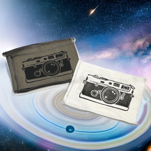 May include: Two rectangular pouches with a black camera design. One pouch is olive green, the other is white. The camera design is a detailed illustration of a vintage camera. The background is a space-themed design with a galaxy and a shooting star.