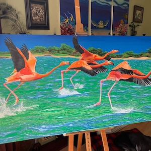 May include: A large painting depicts three flamingos in flight over water. The birds have vibrant orange plumage with black wingtips and long, slender legs. The water is a mix of green and blue, with white splashes. The background shows a shoreline and blue sky.