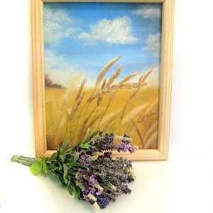 Op de afbeelding: Een ingelijst schilderij van een tarweveld met een blauwe lucht en witte wolken op de achtergrond. Een bosje lavendelbloemen bevindt zich op de voorgrond.