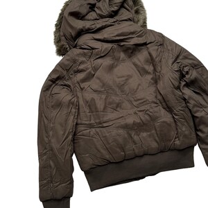 May include: A brown bomber jacket with a faux fur-lined hood. The jacket features a ribbed hem and cuffs, and a quilted design on the back. The jacket is a neutral color and appears to be made of a lightweight material.
