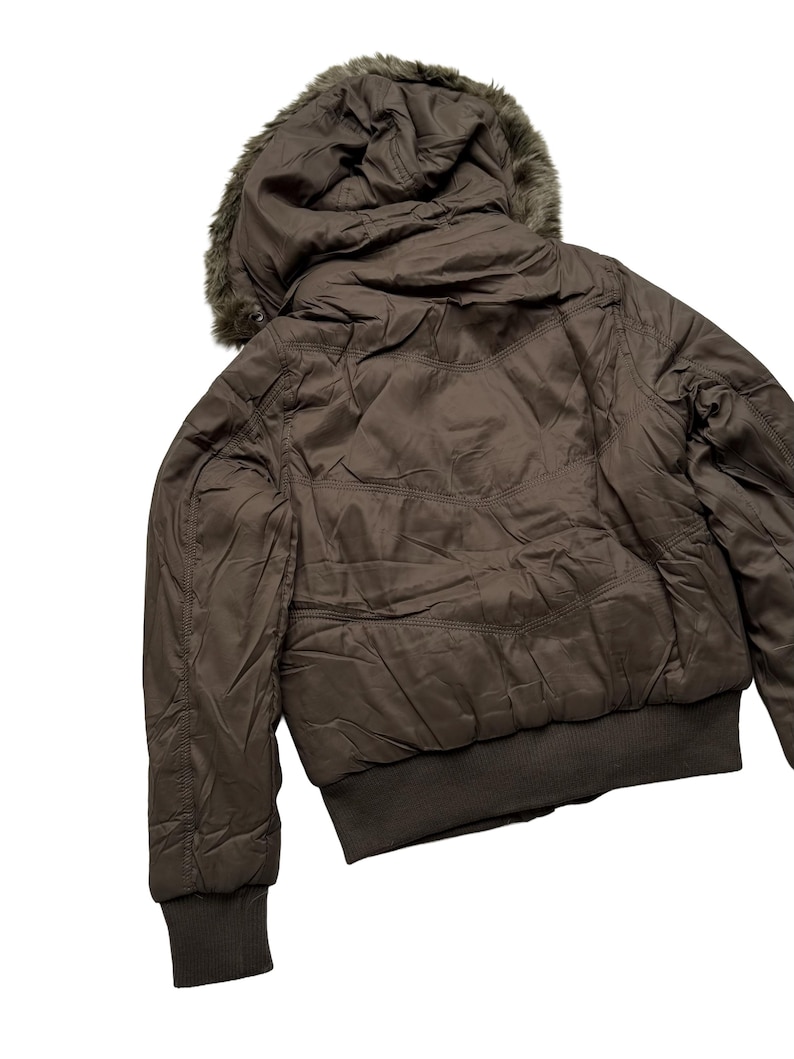 May include: A brown bomber jacket with a faux fur-lined hood. The jacket features a ribbed hem and cuffs, and a quilted design on the back. The jacket is a neutral color and appears to be made of a lightweight material.