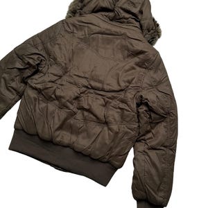 May include: A brown bomber jacket with a hood and faux fur trim. The jacket has a quilted design and a ribbed hem and cuffs. The jacket is shown from the back, with the hood up.