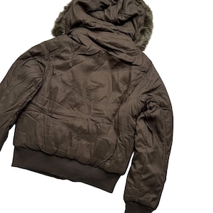 May include: A brown bomber jacket with a faux fur-lined hood. The jacket features a ribbed hem and cuffs, and a quilted design. The jacket is made of a smooth, shiny material.