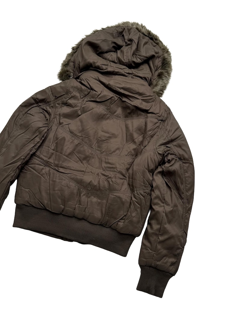 May include: A brown bomber jacket with a faux fur-lined hood. The jacket features a ribbed hem and cuffs, and a quilted design. The jacket is made of a smooth, shiny material.