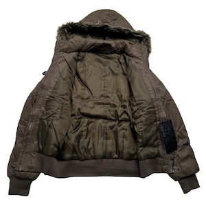 May include: A brown hooded jacket with a faux fur trim around the hood. The jacket has a ribbed hem and cuffs, and a quilted interior. A black label with white text is visible on the right side.