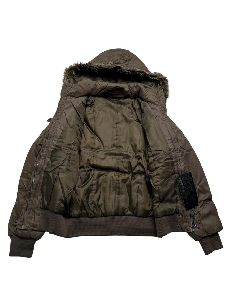May include: A brown hooded jacket with a faux fur trim around the hood. The jacket has a ribbed hem and cuffs, and a quilted interior. A black label with white text is visible on the right side.
