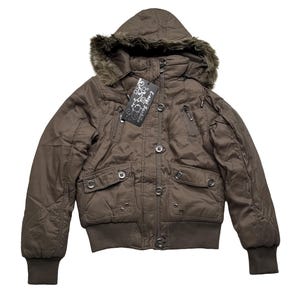 May include: Brown hooded jacket with a faux fur trim around the hood. The jacket has a quilted design, multiple pockets, and a ribbed hem and cuffs. The tag reads "E-migl Fashion".