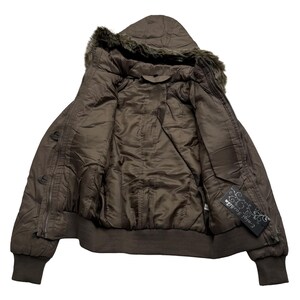 May include: A brown bomber jacket with a hood trimmed with faux fur. The jacket has a zipper closure and ribbed cuffs and hem. The interior lining is a lighter shade of brown. A tag with the text "Ential Fashion" is visible.