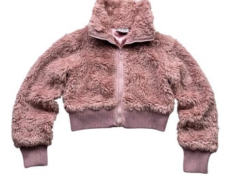 May include: A cropped, dusty rose-colored jacket with a high collar and a full-length zipper. The jacket is made of a soft, fuzzy material and features ribbed cuffs and a ribbed hem. The jacket is a stylish outerwear option.