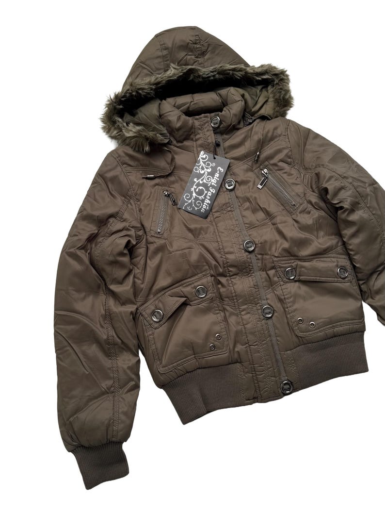 May include: Brown bomber jacket with a hood trimmed with faux fur. The jacket has multiple pockets, a zipper closure, and a ribbed hem and cuffs. A tag with the text "Enlai Fashion" is attached.