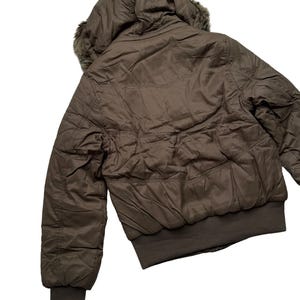 May include: A brown bomber jacket with a hood and faux fur trim. The jacket has a ribbed hem and cuffs. The jacket is made of a quilted material and has a zipper closure. The jacket is a neutral color and can be worn in the fall or winter.
