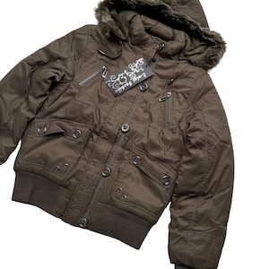 May include: A brown bomber jacket with a fur-lined hood. The jacket has multiple pockets, a ribbed hem and cuffs, and a tag that reads "E-nial Fashion". The jacket is buttoned up and has a quilted design.