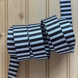 May include: A roll of black and white striped ribbon. The ribbon is tightly wound, with the striped pattern clearly visible. The ribbon is made of a sturdy material and is suitable for various crafting projects.