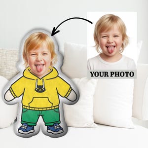 May include: A custom-shaped pillow featuring a child's photo, with a yellow hoodie, green pants, and blue shoes. The pillow is designed to resemble the child's likeness, with a playful expression. A separate photo with the text "YOUR PHOTO" is also included.