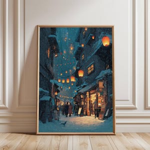 May include: A framed art print depicts a snowy street scene at night. Buildings line the street, with orange lanterns illuminating the path. People are walking along the street. The artwork is framed in a gold-colored frame and is displayed on a wooden floor.