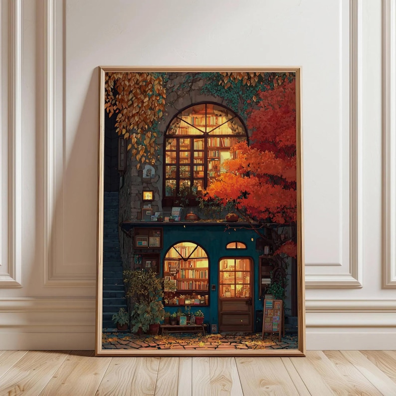 May include: A framed print of a cozy bookstore scene. The building has a teal facade, arched windows, and is surrounded by autumn foliage in shades of orange and gold. Bookshelves are visible through the windows, and the scene is warmly lit.