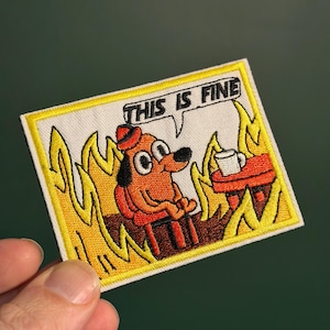 May include: Embroidered patch depicting a cartoon dog in a burning room, with the text "THIS IS FINE" in a speech bubble. The dog is brown with a red hat, and the flames are yellow and orange. A small table with a coffee cup is also present.
