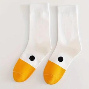 May include: A pair of white socks with yellow toes and a black dot on the side. The socks are made of a soft material and are designed to be comfortable. The socks are a fun and quirky accessory.