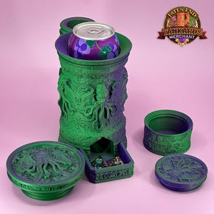 Könnte beinhalten: Ein grüner und violetter Würfelturm mit passender Würfelschale und zwei Deckeln. Im Turm befindet sich eine Getränkedose. Der Turm und das Zubehör sind mit aufwendigen Designs verziert, vor rosa Hintergrund.