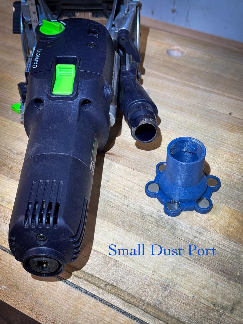 May include: A dark blue power tool with green accents and the word "DOMINO" printed on the side. A blue small dust port is next to the tool. The text "Small Dust Port" is printed in blue.