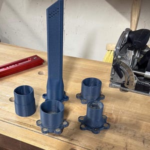 May include: A collection of blue 3D-printed woodworking tools and accessories. The set includes a tall, slender nozzle with air vents, several cylindrical attachments, and a red metal angle measuring tool. A black and green power tool is also visible.