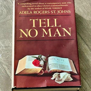 Può includere: Un libro con copertina rigida intitolato Tell No Man di Adela Rogers St. Johns con una copertina rosso scuro. La parte anteriore presenta un libro aperto che mostra The Acts, una singola rosa rossa e un fazzoletto di pizzo bianco.