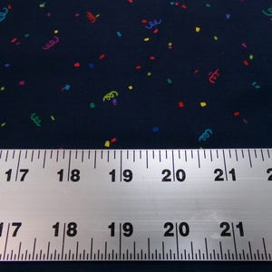 May include: Dark navy fabric with a colorful confetti pattern. The fabric is decorated with small, multi-colored rectangles and curly ribbon shapes. A metal ruler with inch measurements is placed across the fabric.