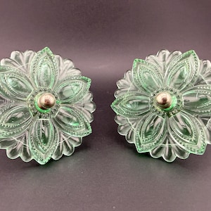 May include: Two round, light green glass drawer knobs featuring a pressed floral petal design with intricate beaded detailing along the edges. Each knob has a central silver-toned metal hardware component at the core of the flower shape.