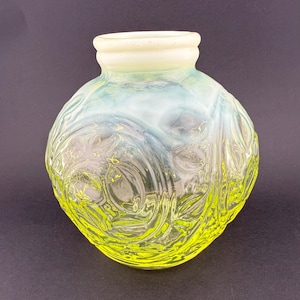May include: A decorative glass vase with a round body and a short neck. The vase features a floral pattern and a gradient of colours, transitioning from a bright yellow base to a pale blue and white top. The rim is a creamy white.