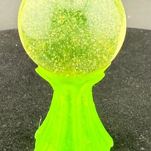 Op de afbeelding: Een neon groene decoratieve bol met een getextureerd, gespikkeld oppervlak, rustend op een bijpassende voet. De voet heeft een uitlopend, gestileerd ontwerp. De algehele esthetiek is modern en opvallend.