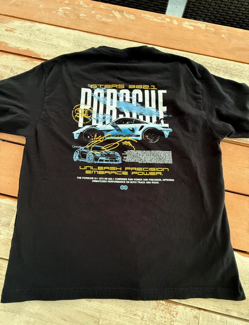 May include: A black t-shirt featuring a graphic on the back with the text PORSCHE, GT3RS 992.1, UNLEASH PRECISION EMBRACE POWER, and a detailed description of the Porsche 911 GT3 RS 992.1, accompanied by illustrations of the sports car.