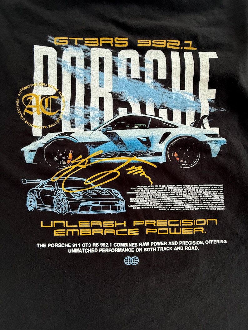 May include: A black t-shirt featuring a graphic of a light blue Porsche 911 GT3 RS 992.1. The design includes the text PORSCHE, GT3 RS 992.1, UNLEASH PRECISION EMBRACE POWER, and a detailed paragraph about the vehicle's performance specifications.