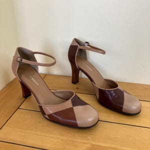 May include: A pair of Nine West heeled shoes with ankle straps. The shoes feature a colour block design with brown, tan, and beige leather. The heels are approximately 7.6 cm high.