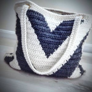 May include: A white and gray crocheted tote bag with a chevron pattern. The bag has two long straps.