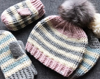 May include: A set of striped knit winter accessories including a hat with a faux fur pom pom, a pair of mittens, and a fingerless mitten.