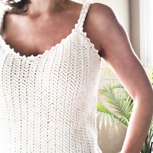 Puede incluir: Un top blanco de crochet sin mangas con escote festoneado y tirantes finos.