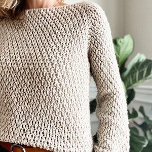 May include: A beige knitted sweater with a loose fit and long sleeves. The sweater has a textured stitch pattern.