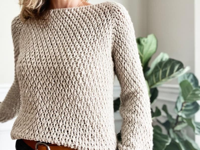 May include: A beige knitted sweater with a loose fit and long sleeves. The sweater has a textured stitch pattern.