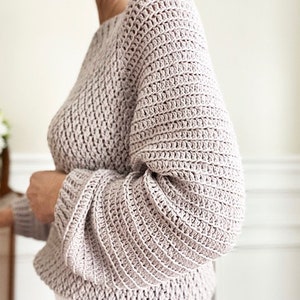 May include: A soft, light pink crocheted sweater with long sleeves and a relaxed fit.