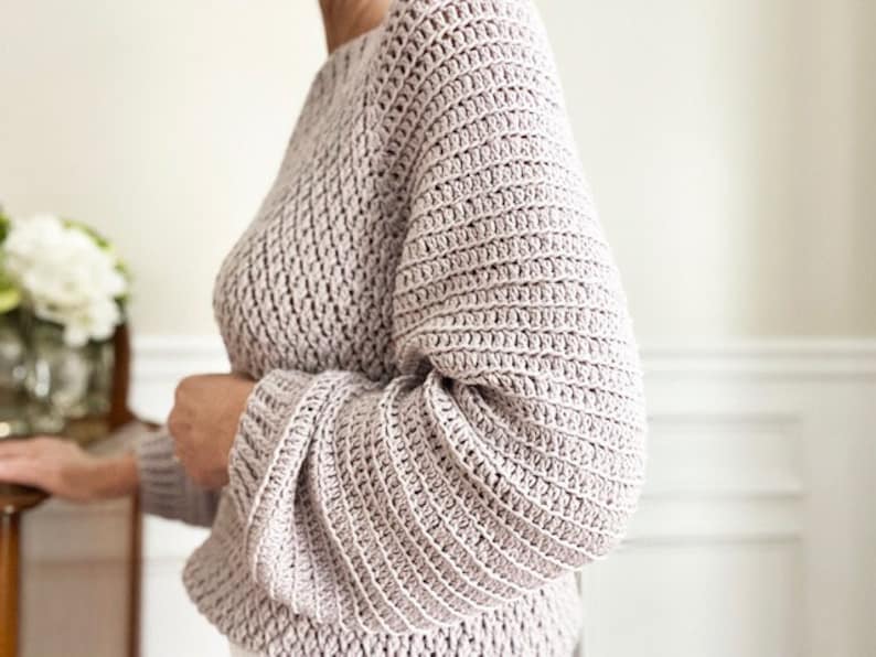 May include: A soft, light pink crocheted sweater with long sleeves and a relaxed fit.