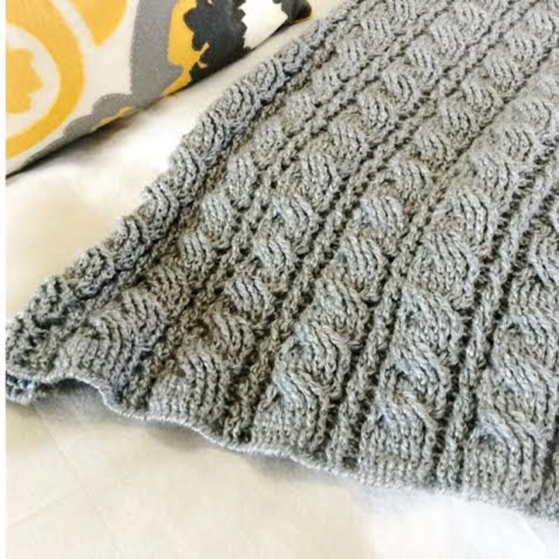 Puede incluir: Una manta de ganchillo gris con un patr&oacute;n texturizado. La manta est&aacute; hecha con un hilo suave y tiene un dise&ntilde;o delicado e intrincado.