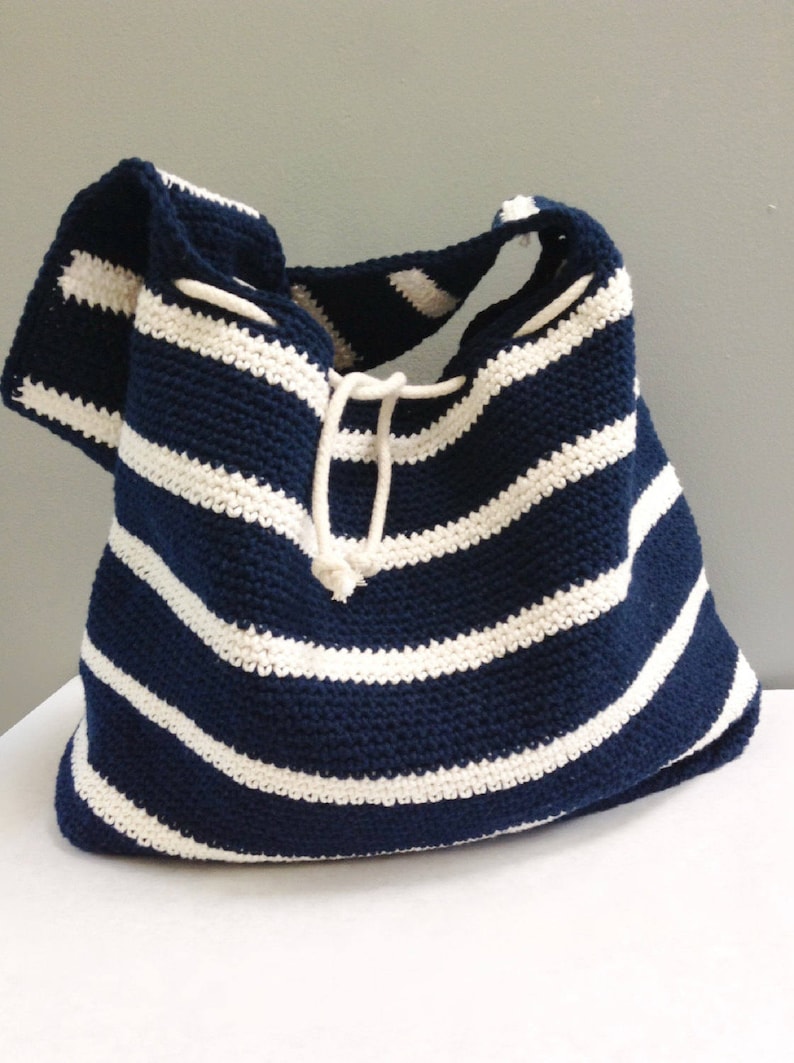 May include: A navy blue and white striped crocheted tote bag with a drawstring closure.