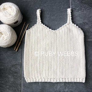 Puede incluir: Un top blanco de crochet con tirantes finos y un escote festoneado. El top est&aacute; hecho con un patr&oacute;n de punto simple y tiene un ajuste holgado.