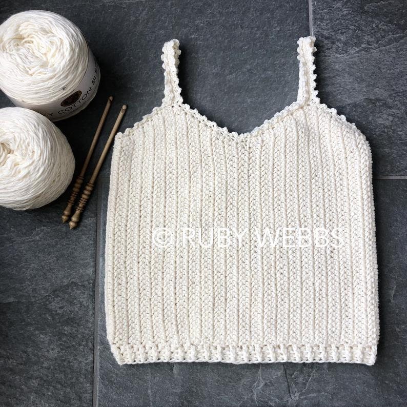 Puede incluir: Un top blanco de crochet con tirantes finos y un escote festoneado. El top est&aacute; hecho con un patr&oacute;n de punto simple y tiene un ajuste holgado.